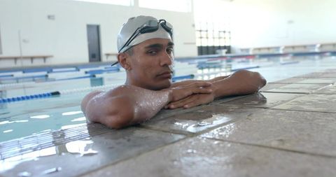 Competitive swimmer resting at pool edge with goggles and silver swim cap