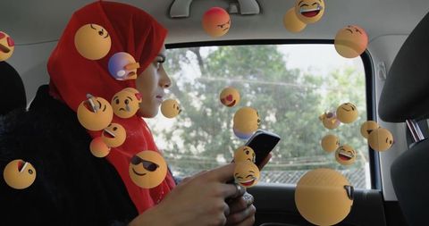 Woman in red hijab using smartphone surrounded by emojis