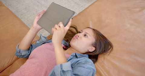 Teen girl engaged with tablet on sofa relaxing at home