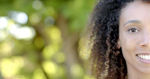 Half Portrait of Smiling Biracial Woman with Curly Hair in Sunny Garden