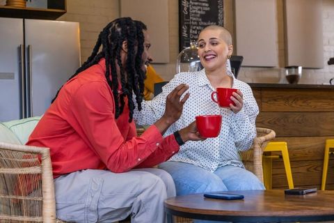 African american man and woman laughing, holding red mugs, chatting in cozy coffeehouse
