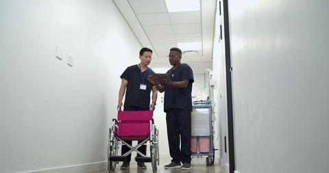 Clinical staff reviewing tablet in hospital corridor with magenta wheelchair