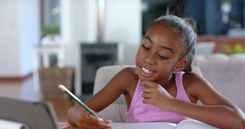 African american girl studying at home writing in notebook with laptop