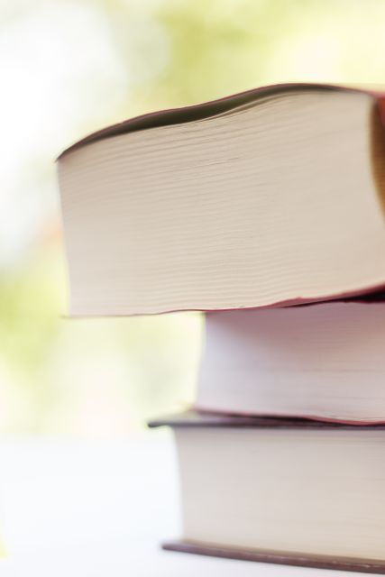 Close-up view of a stack of thick hardcover books with a blurred background. This can be used for educational or academic content, promoting literacy and reading, library posters, or articles about literature and book reviews.