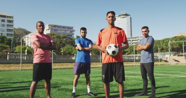 Men standing on soccer field with one holding ball, showcasing confidence and teamwork. Ideal for sports advertising, team-building promotions, or articles on outdoor activities and physical fitness.