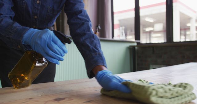 Midsection of person wearing gloves and apron disinfecting tables at cafe bar. work at an independent bar business during coronavirus covid 19 pandemic.