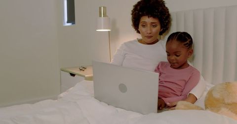 Mother and Daughter Watching Laptop Together in Cozy Bedroom Setting
