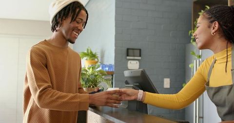 Smiling barista handing coffee to african american customer in cozy plant-filled urban cafe