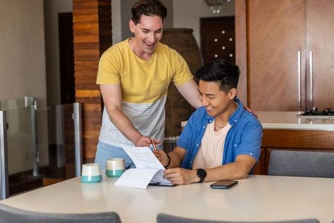 Young diverse men reviewing documents and signing forms at home kitchen table