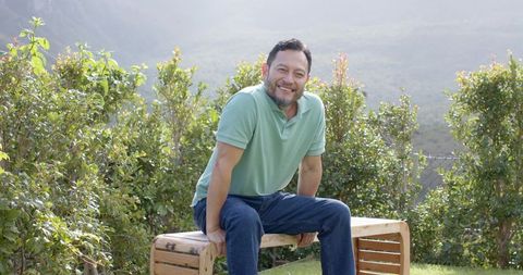 Asian Man Relaxing on Wooden Bench in Tranquil Garden Setting