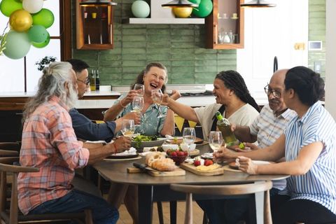 Multigenerational group laughing and toasting at home dining table with wine and food