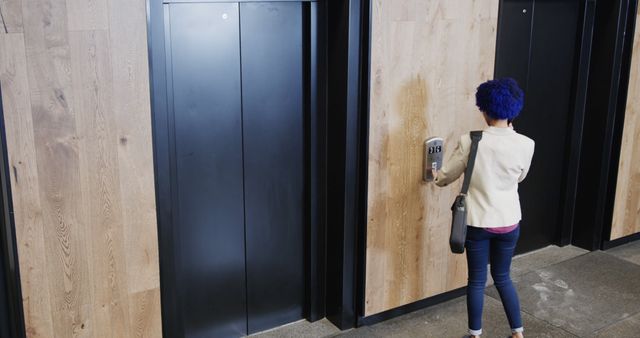 Woman with blue hair standing in front of elevator pressing button. Wearing business attire and carrying bag. Makes use of themes like modern technology, professional daily routine, and urban lifestyle. Great for corporate blogs, technology advertisements, and business presentations.