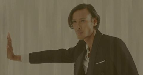 Stylish man pressing sheer curtain in minimalistic studio