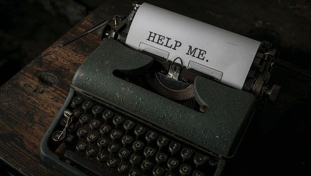 Moody vintage green typewriter typing 'help me.' on cracked wooden desk closeup