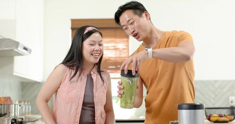 Couple preparing green smoothie in bright modern kitchen for healthy morning routine