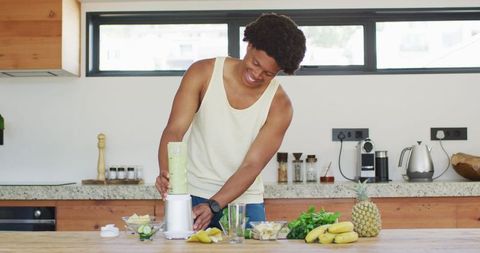 Young Man Making Healthy Green Smoothie in Modern Kitchen