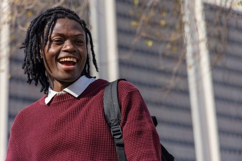 African american man laughing in maroon sweater with backpack in modern urban plaza