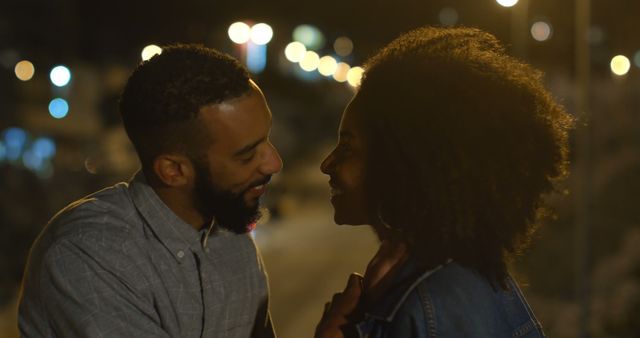 Romantic diverse couple standing close and talking in city street at night, copy space. City living, romance, love, relationship, free time and lifestyle, unaltered.