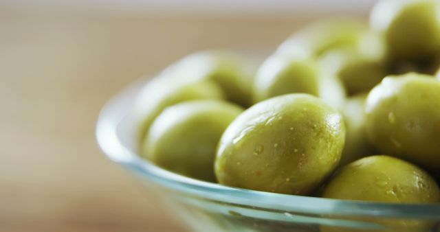 Image showcases a close-up view of fresh green olives in a glass bowl. Perfect for use in advertisements, food blogs, recipes, Mediterranean cuisine promotions, or healthy eating campaigns emphasizing organic and gourmet ingredients.