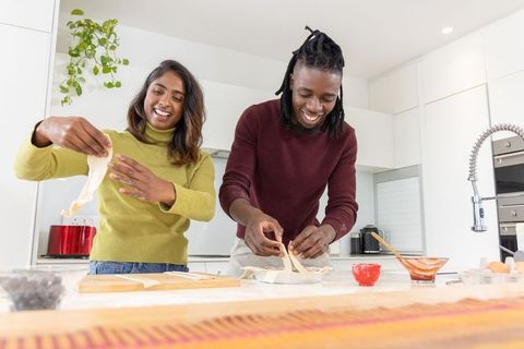 Diverse couple baking pastry together in modern kitchen preparing tart strips and dough
