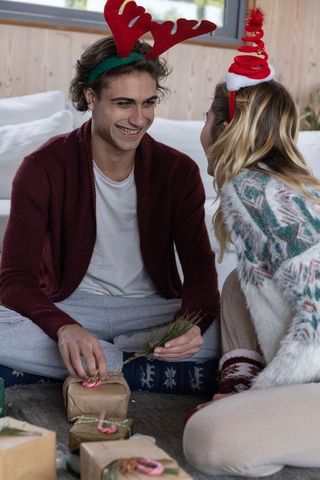 Happy couple with festive headbands unwrapping presents in cozy living room
