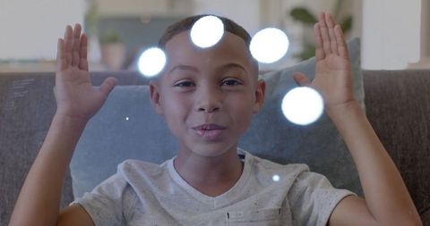 Black boy touching glass while playing with light reflections on living room couch