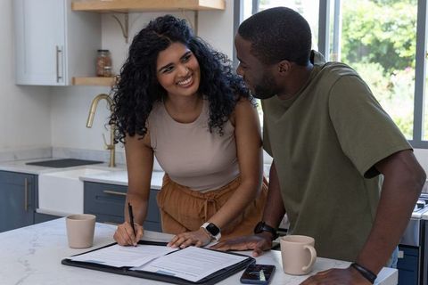 Diverse couple signing home purchase documents on modern kitchen island, smiling together
