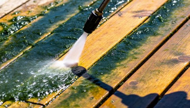 Pressure washing wooden deck planks removing green algae and restoring warm wood tones