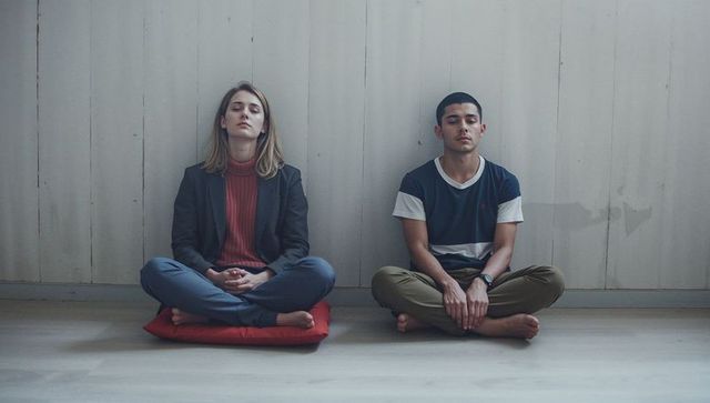 Two adults practicing meditation in minimalist interior with muted tones and soft lighting