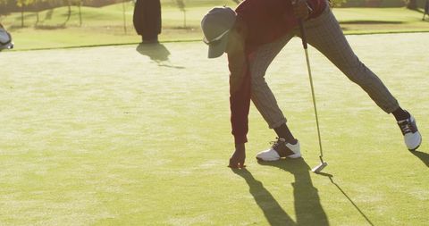 Golf player setting ball on sunny green field