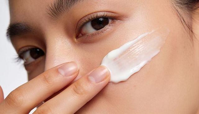 Applying moisturizer close-up asian woman spreading facial cream for glowing skin