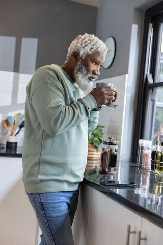 Senior african american man savoring morning coffee at sunlit kitchen window with french press