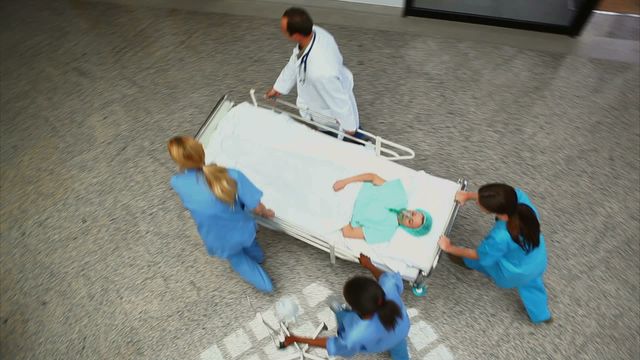 Medical professionals are wheeling a patient on a hospital bed through a corridor at a hospital. This video can be used for illustrating urgent healthcare situations, emergency medical services, hospital staff teamwork, or promotional content for healthcare services.