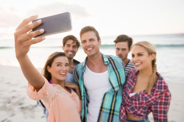 Group of friends enjoying a sunny day at the beach, capturing memories with a selfie. Perfect for promoting summer vacations, travel destinations, friendship, and outdoor activities. Ideal for use in social media campaigns, travel blogs, and lifestyle advertisements.
