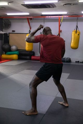 Mature african american man training boxing and footwork in gym with heavy bags