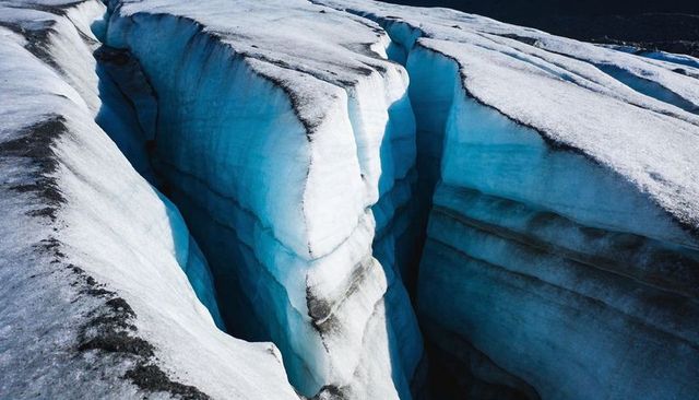 Deep glacier crevasse revealing stratified blue ice and dark moraine bands