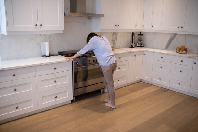 Woman standing in a modern kitchen with white cabinets and a marble backsplash, appearing worried or stressed. Suitable for use in articles or advertisements related to mental health, stress management, home life, or kitchen design.