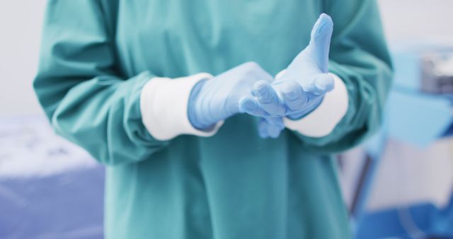 Image of midsection of surgeon wearing surgical gloves and gown in operating theatre. Hospital, medical and healthcare services.