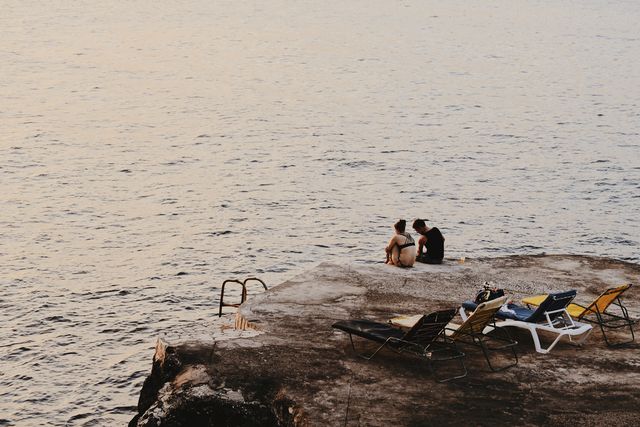 Couple Sitting on Concrete Pier by Serene Ocean During Sunset - Download Free Stock Photos Pikwizard.com