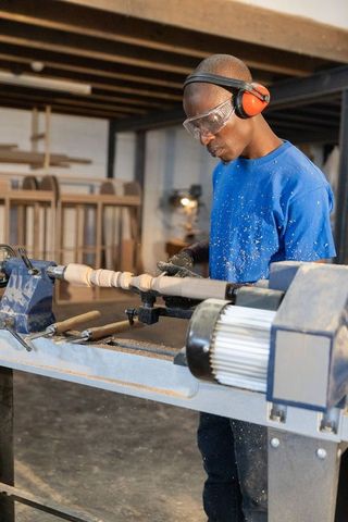 Woodworker shaping spindle on lathe wearing safety gear, precision woodturning