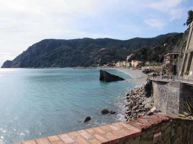 Coastal view of Monterosso Al Mare in Italy, featuring rocky shoreline and clear blue waters with cliffs in the background. Perfect for use in travel blogs, tourism advertisements, and destination guides showcasing scenic beauty and coastal landscapes.