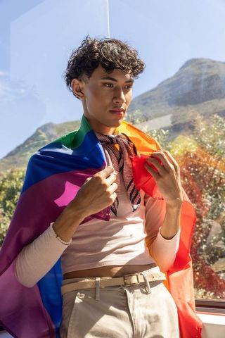 Peaceful individual expressing pride with rainbow flag by sunlit cabin