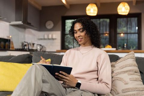 Non-binary person journaling on sofa in cozy modern living room wearing pink sweater