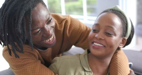 African American couple laughing and cuddling on sofa in sunlit cozy home interior