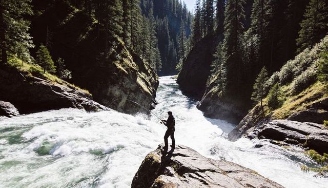 Solitary angler casting over roaring canyon river from rocky ledge, wilderness adventure