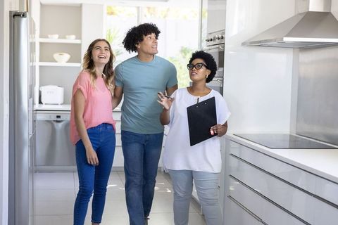 Young couple touring modern kitchen with african american agent holding clipboard