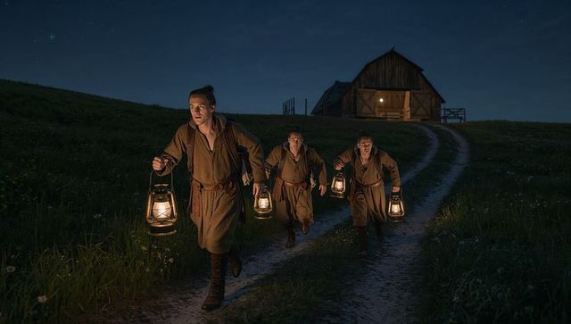 Men carrying lanterns on night patrol up lane toward illuminated barn period reenactors