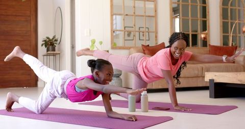 African american mother and daughter practicing yoga in pink activewear, bright living room