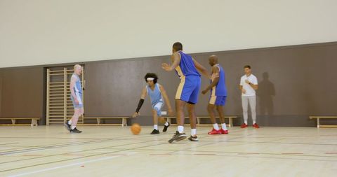 Indoor basketball scrimmage with male players dribbling, defending on school gym court