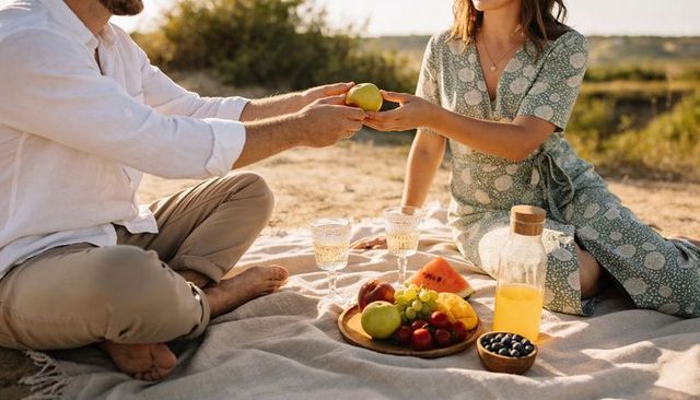 Sunlit picnic couple sharing fruit on blanket outdoors romantic summer meadow moment